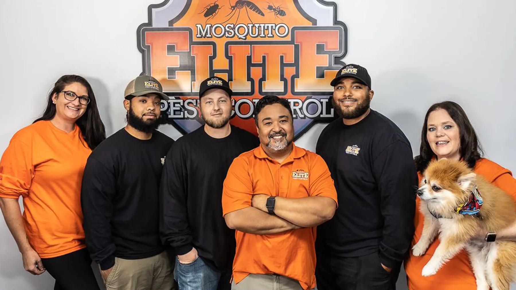 The Mosquito Elite Pest Control team in their orange and black shirts standing in front of the company sign